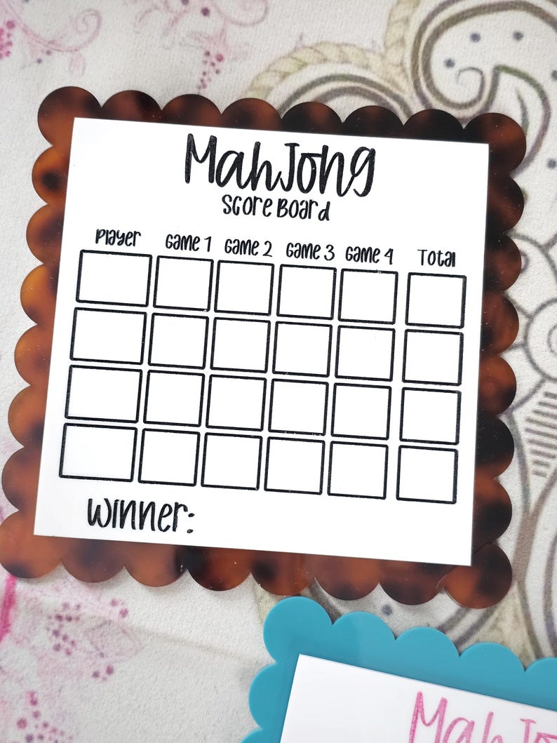 May include: A Mahjong score board with a brown tortoiseshell scalloped border. The white center has the words "Mah Jong Score Board" and boxes to record player scores for each game. The word "Winner:" is at the bottom.