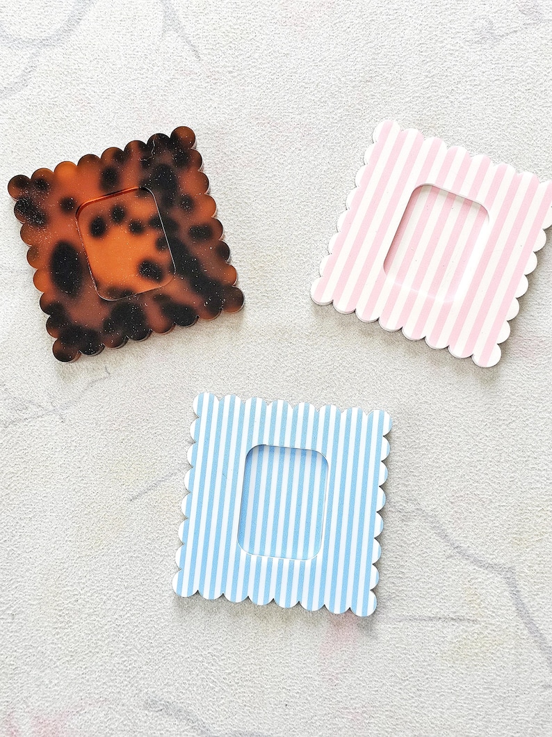 Puede incluir: Tres marcos cuadrados decorativos con bordes festoneados. Uno tiene un patr&oacute;n de carey, los otros dos presentan rayas verticales en rosa y azul. Cada marco tiene una abertura rectangular en el centro.