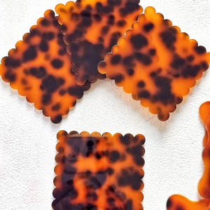 May include: Several tortoise shell-patterned hair clips with scalloped edges. The clips are square and rectangular, featuring a mottled pattern of brown and amber. The clips are made of a shiny, smooth material.