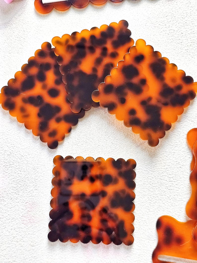 May include: Several tortoise shell-patterned hair clips with scalloped edges. The clips are square and rectangular, featuring a mottled pattern of brown and amber. The clips are made of a shiny, smooth material.