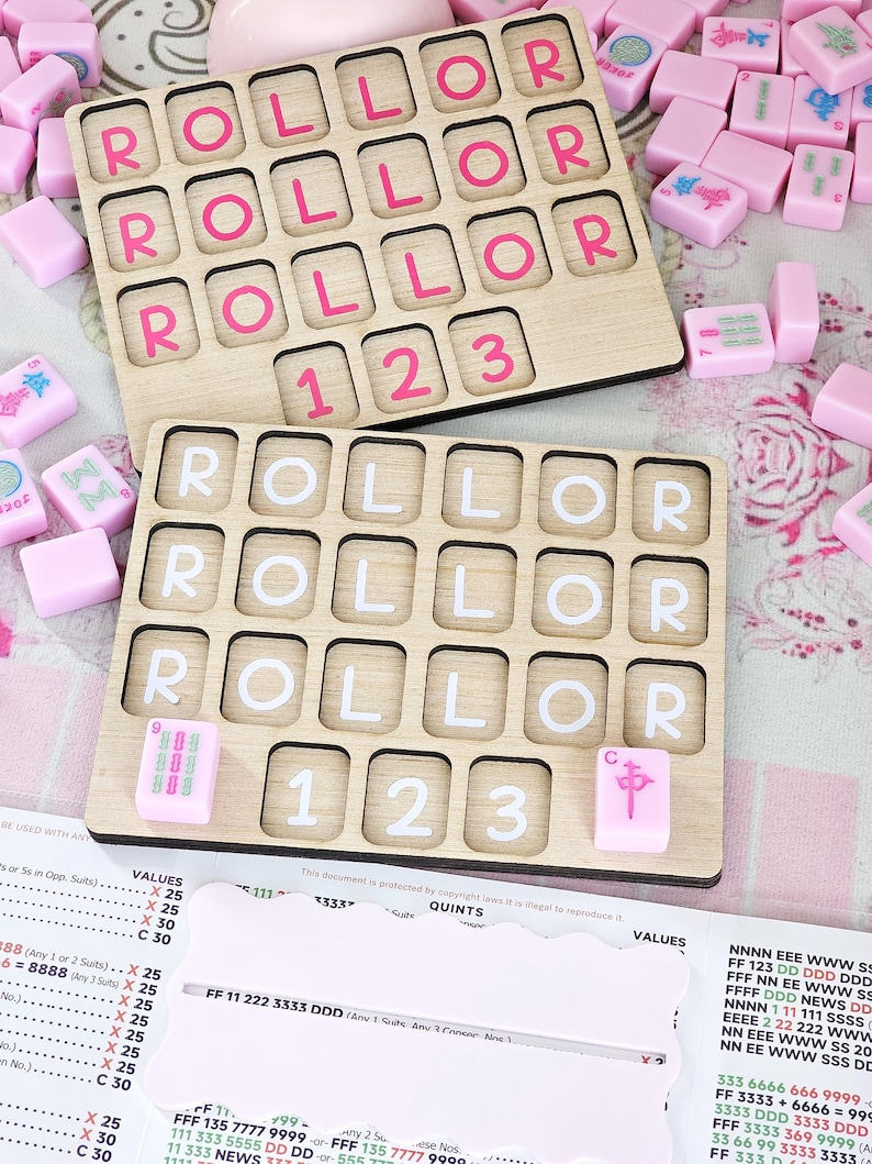 May include: Two rectangular wooden game boards with grid cutouts, each featuring the word ROLLOR and the numbers 1 2 3. The top board has pink lettering, while the bottom board has white lettering. Scattered pink mahjong tiles surround the boards.