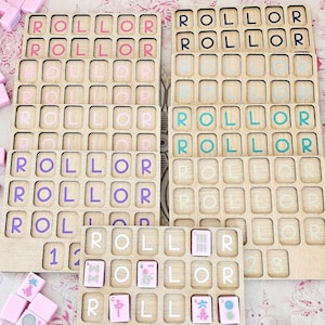 May include: A set of wooden game boards with grid slots for tiles, featuring the word ROLLOR printed in various colors including pink, purple, teal, and white. Some boards contain scattered pink mahjong-style tiles with symbols and numbers.