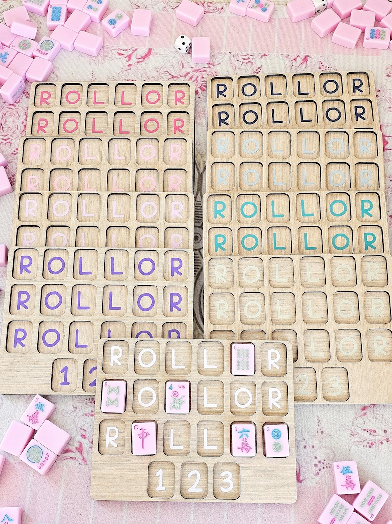 May include: A set of wooden game boards with grid slots for tiles, featuring the word ROLLOR printed in various colors including pink, purple, teal, and white. Some boards contain scattered pink mahjong-style tiles with symbols and numbers.