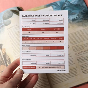 May include: A white card titled "BARBARIAN RAGE + WEAPON TRACKER" with a chart for tracking game stats. The card is held over an open book with illustrations. The chart includes sections for Rage Damage, Rage Count, and Weapon Name.