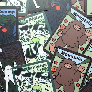 May include: A collection of rectangular playing cards featuring colorful cartoon illustrations of creatures and landscapes. The cards include labels such as Swamp, Plains, Mountain, Forest, and Island, with depictions of a brown yeti, cows, and ghosts.