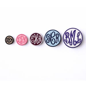 May include: Five circular embroidered patches arranged in a row from smallest to largest. Each patch features a unique three-letter monogram in a cursive script. The colors include black, pink, maroon, light blue, and white with purple stitching.