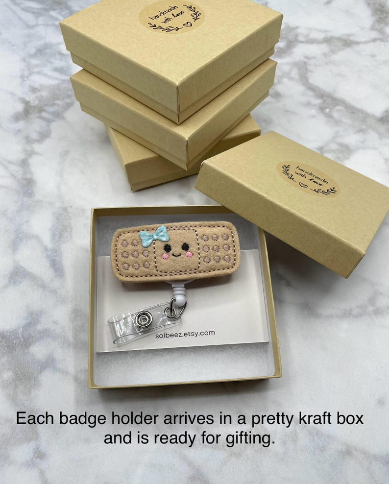 A handmade badge holder with a smiley face and a clear plastic keychain attached to it, placed in a cardboard box.