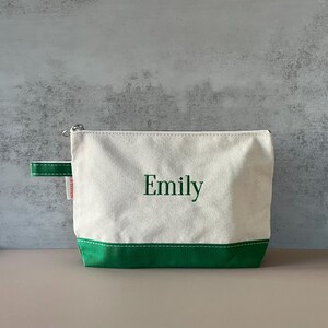 Peut inclure: Une trousse de toilette en toile avec un corps blanc et une base et une poign&eacute;e vertes. Le nom "Emily" est brod&eacute; en vert sur le devant. Le sac a une fermeture &eacute;clair argent&eacute;e.