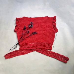May include: A vibrant red crochet top with a tie closure. The top features a textured stitch pattern, ruffled edges, and a decorative openwork design along the bottom. The text "MUTO_CROCHET" is visible on the right side.