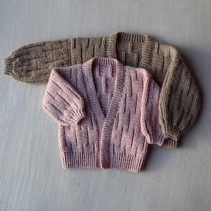 May include: Two knitted cardigans, one in a light pink color and one in a brown color. Both cardigans have a cable knit pattern and a v-neck.