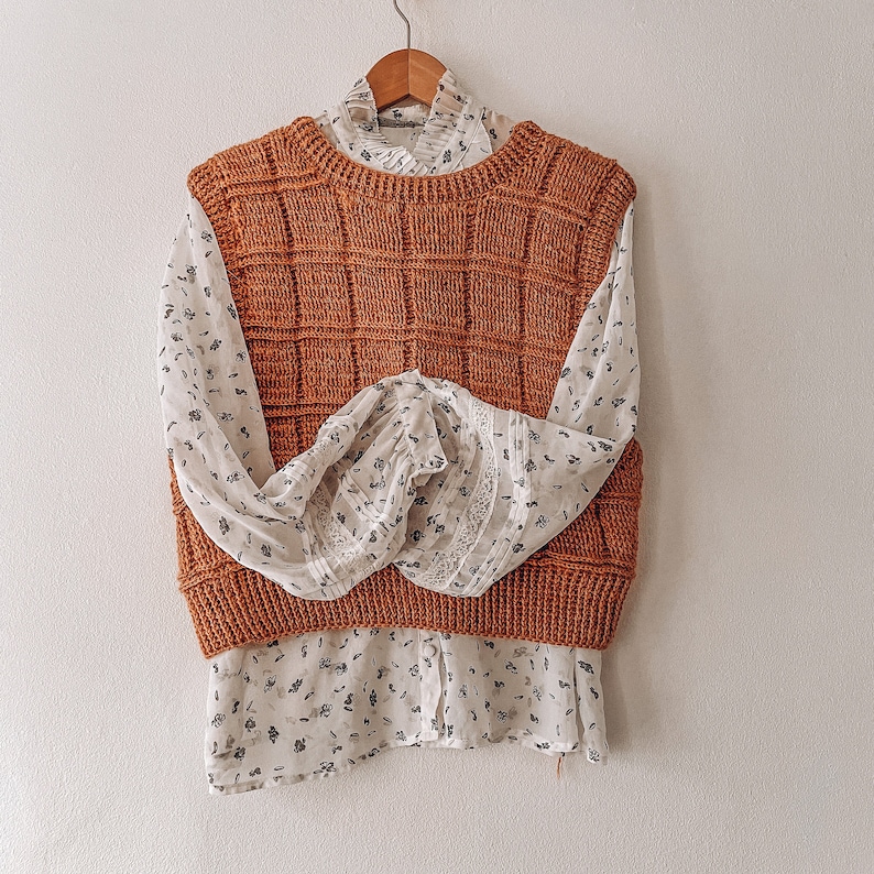 May include: A brown crocheted vest with a white blouse underneath. The blouse has a floral pattern and lace trim.