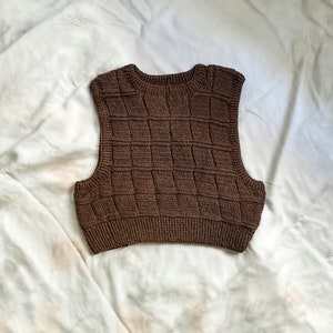 May include: A brown sleeveless knitted vest with a square pattern.