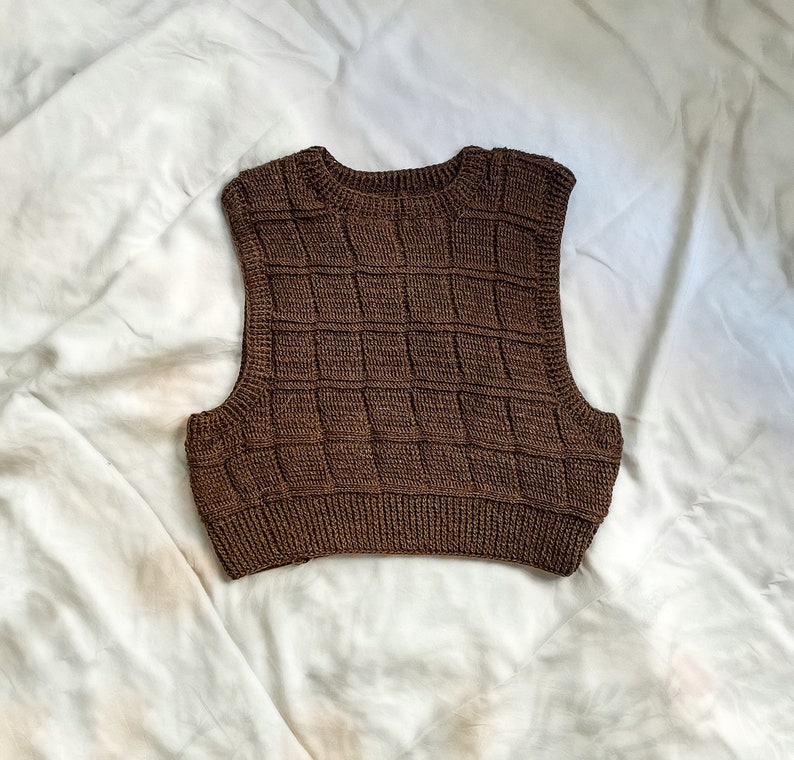 May include: A brown sleeveless knitted vest with a square pattern.