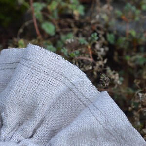 May include: Close-up of folded, light beige linen fabric with a raw edge. The fabric is textured and has visible stitching along the edge. The words "Raw edge" are in the top right corner.