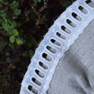 May include: Close-up of a white ribbon with a scalloped edge, featuring a series of oval cutouts. The ribbon is sewn onto a light grey fabric. The word "Ribbon" is visible in the upper left corner.