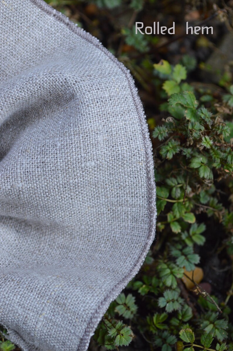 May include: A white ceramic mug with a black handle and the text "But First, Coffee" in a bold, black font. The mug is set against a blurred background. The mug appears to be approximately 10 cm tall.