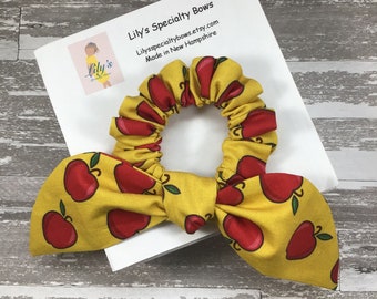 May include: A yellow scrunchie with a red apple print. The scrunchie is tied in a bow and is made of fabric. The scrunchie is on a white background with text that reads "Lily's Specialty Bows Lilysspecialtybows.etsy.com Made in New Hampshire".