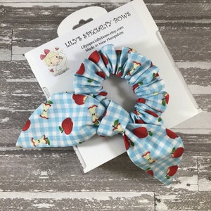 May include: A blue and white gingham hair scrunchie with red apple print. The scrunchie is tied in a bow and is packaged on a white card with the text "Lily's Specialty Bows" and "Lilysspecialtybows.etsy.com Made in New Hampshire".