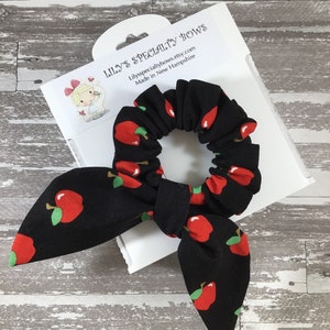 May include: Black scrunchie with a red apple print. The scrunchie is tied in a bow and is on a white card with the text "Lily's Specialty Bows" and "Lilysspecialitybows.etsy.com Made in New Hampshire".