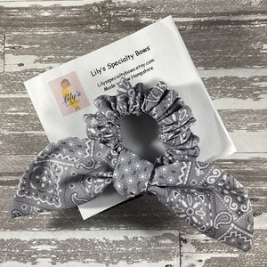 May include: Gray and white bandana print scrunchie with a bow. The scrunchie is made by Lily's Specialty Bows, and the text "Lily's Specialty Bows" and "Lilyspecialtybows.etsy.com" is printed on a white card behind the scrunchie.