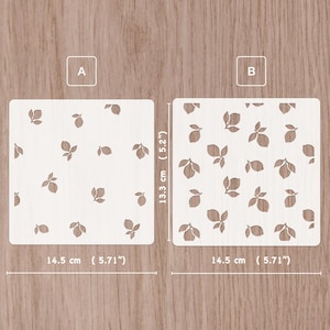May include: Two square stencils labeled A and B, featuring a repeating lemon and leaf pattern. Each stencil measures 13.3 cm by 14.5 cm (5.2 inches by 5.71 inches). The stencils are white with cutouts that reveal the wood grain surface underneath.
