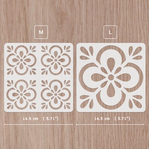May include: Two white plastic stencils with a floral design. The stencil on the left is labelled "M" and measures 5.71 inches square. The stencil on the right is labelled "L" and measures 5.71 inches square.