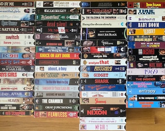 May include: A collection of numerous VHS tapes arranged in four vertical columns. Each spine features distinct movie titles such as Stand By Me, Seabiscuit, Meet Joe Black, and Nixon, displayed in various fonts and colors against diverse background designs.