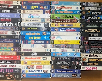 May include: A collection of numerous VHS tapes arranged in four vertical columns. Each tape features a distinct spine with movie titles such as Mission: Impossible, Top Gun, Snatch, Gladiator, Casino, and various others, displaying colorful text and graphics.