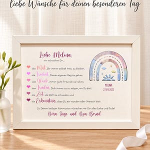 May include: A white rectangular frame containing a personalized print for a First Communion. The print features the text 'Liebe Melina', a list of wishes with heart icons, a watercolor-style rainbow illustration, and the name 'MELINA' with the date '27.04.2025'.