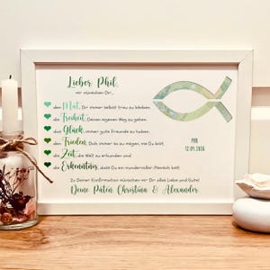 Könnte beinhalten: Gerahmter Druck mit grünem Text und Fischsymbol. Der Text enthält einen Namen, Wünsche und ein Datum. Der Druck befindet sich in einem weißen Rahmen und wird auf einer Holzoberfläche angezeigt.