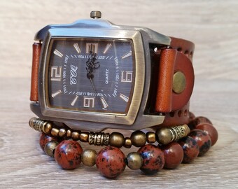 May include: A square-shaped watch with a brown leather band and a silver face. The watch is surrounded by a brown beaded bracelet.