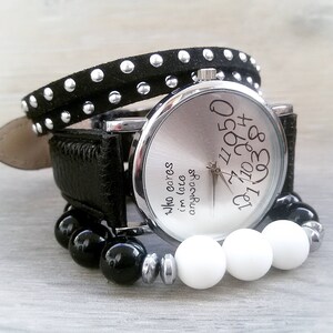 May include: A silver wristwatch with a black leather band and black studded bracelet. The watch face has white numbers and the text "Who cares I'm late anyways".