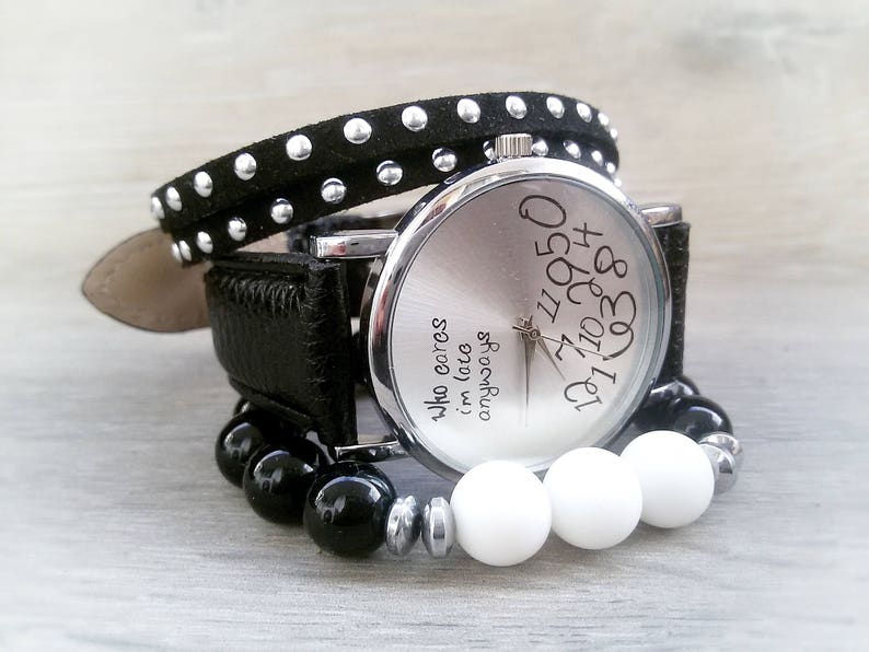 May include: A silver wristwatch with a black leather band and black studded bracelet. The watch face has white numbers and the text "Who cares I'm late anyways".