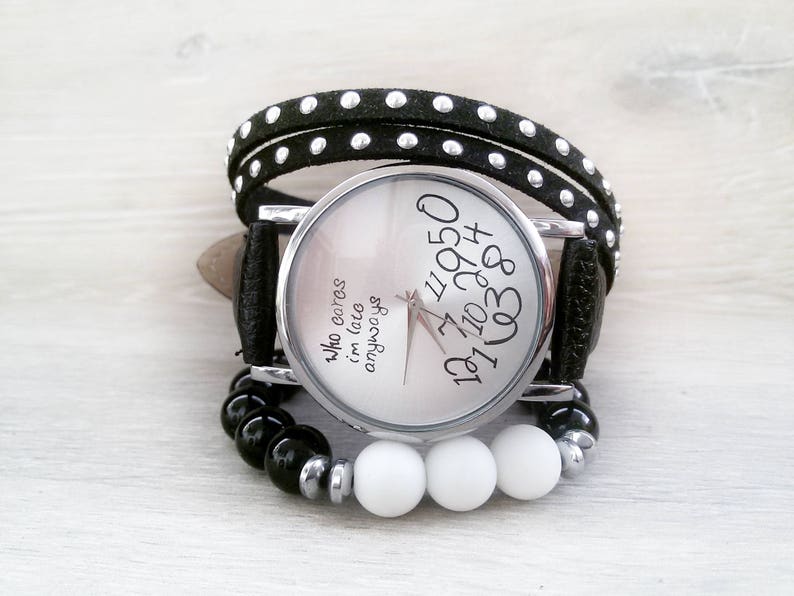 May include: A black and white wristwatch with a black leather band and white beads. The watch face has the text "Who cares I'm late anyways" and numbers around the edge.