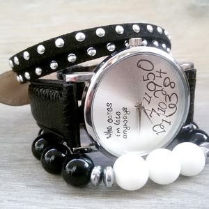 May include: A silver wristwatch with a black leather band and black and white beads. The watch face has the text "8301 410 42950" and "Who cares im late anyway" printed on it.