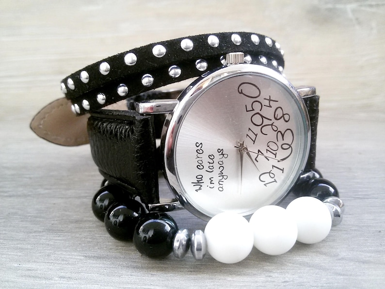 May include: A silver wristwatch with a black leather band and black and white beads. The watch face has the text "8301 410 42950" and "Who cares im late anyway" printed on it.