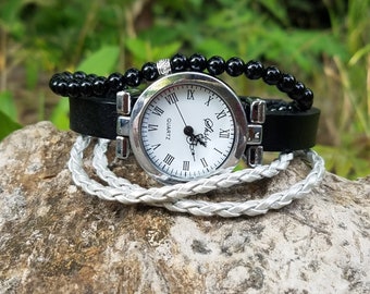 May include: A silver watch with a white face and black roman numeral hour markers. The watch has a black leather band and is wrapped with a white braided cord.