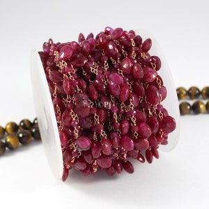 Op de afbeelding: Een spoel met robijnrode edelsteen kralen geregen aan een gouden ketting. De kralen zijn ovaalvormig en hebben een facetgeslepen oppervlak.