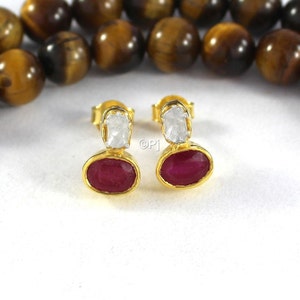 May include: A pair of gold earrings with a red oval gemstone and a white diamond-shaped gemstone.