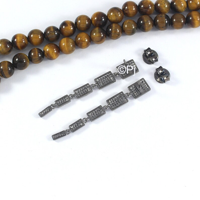 May include: A pair of long, silver dangle earrings with multiple rectangular-shaped stones. The stones are set in a pave setting and have a sparkly finish. The earrings are hanging from a silver post with a butterfly back.