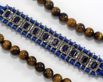 May include: A blue cord bracelet with a silver and blue gemstone design. The bracelet is accented with small, clear gemstones.