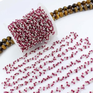 May include: A spool of silver chain with pink gemstone beads. The chain is made of small, delicate links and the beads are faceted and have a slightly irregular shape. The chain is perfect for making jewelry or other crafts.