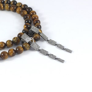 May include: A pair of dangle earrings with a silver chain and rectangular stones set with small diamonds. The earrings are displayed on a brown and gold tiger's eye beaded necklace.