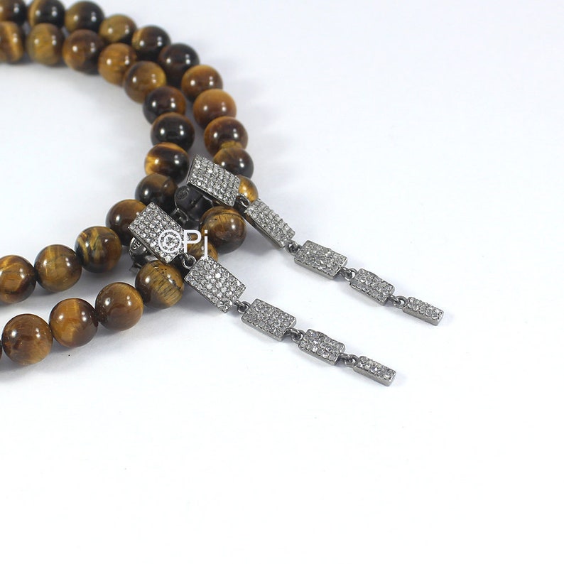 May include: A pair of dangle earrings with a silver chain and rectangular stones set with small diamonds. The earrings are displayed on a brown and gold tiger's eye beaded necklace.