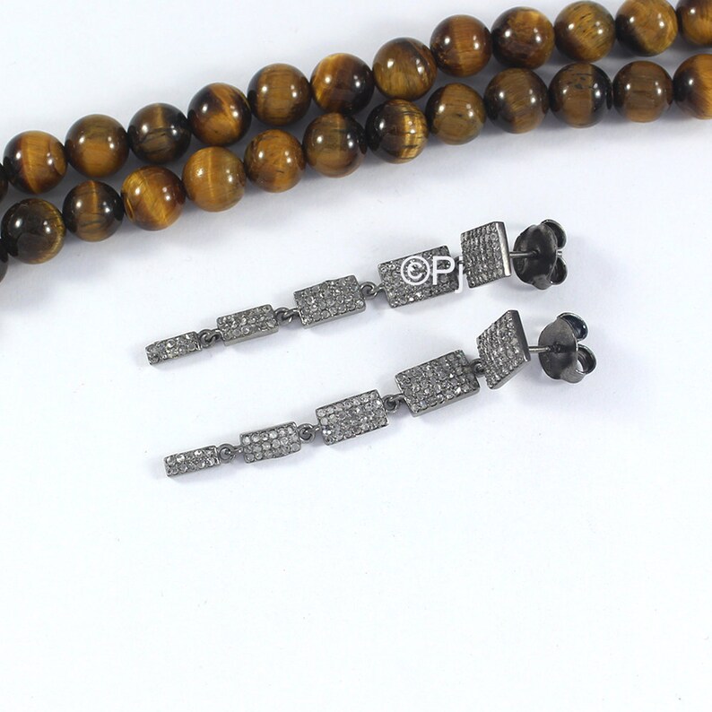 May include: A pair of long silver dangle earrings with a row of small square-shaped stones. The stones are set in a silver frame and are connected by a thin silver chain.