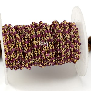 May include: A spool of gold chain with ruby red beads. The chain is made of small, delicate links and the beads are faceted.