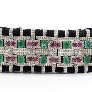 Op de afbeelding: Een zwarte en zilveren armband met een geometrisch ontwerp. De armband is versierd met smaragdgroene en robijnrode edelstenen.