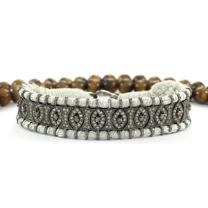 Pode incluir: Um bracelete trançado branco com um fecho prateado e uma fila de formas ovais encrustadas com diamantes pretos.