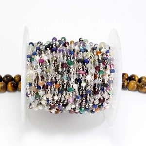 May include: A spool of silver chain with assorted gemstone beads. The beads are in various colours, including blue, green, red, and purple. The chain is made of small, silver links.