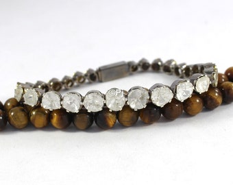 May include: A silver bracelet with a row of clear round stones and a tiger's eye bead bracelet.